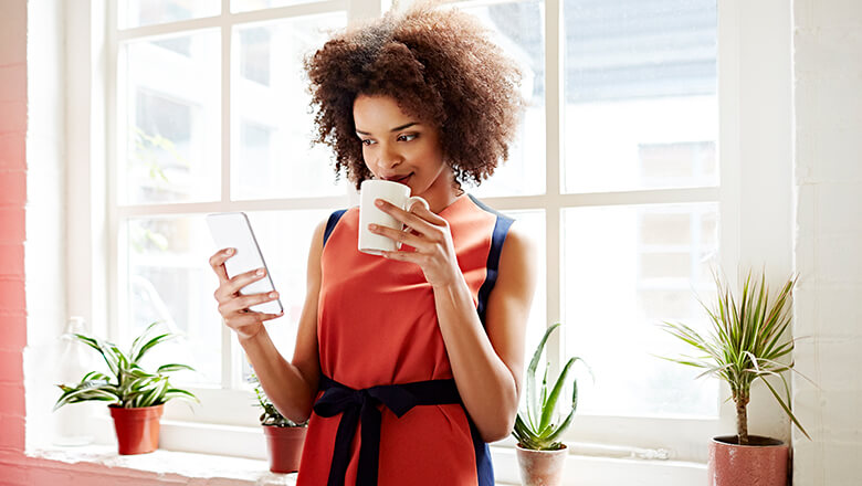 Woman on smartphone with mug at window