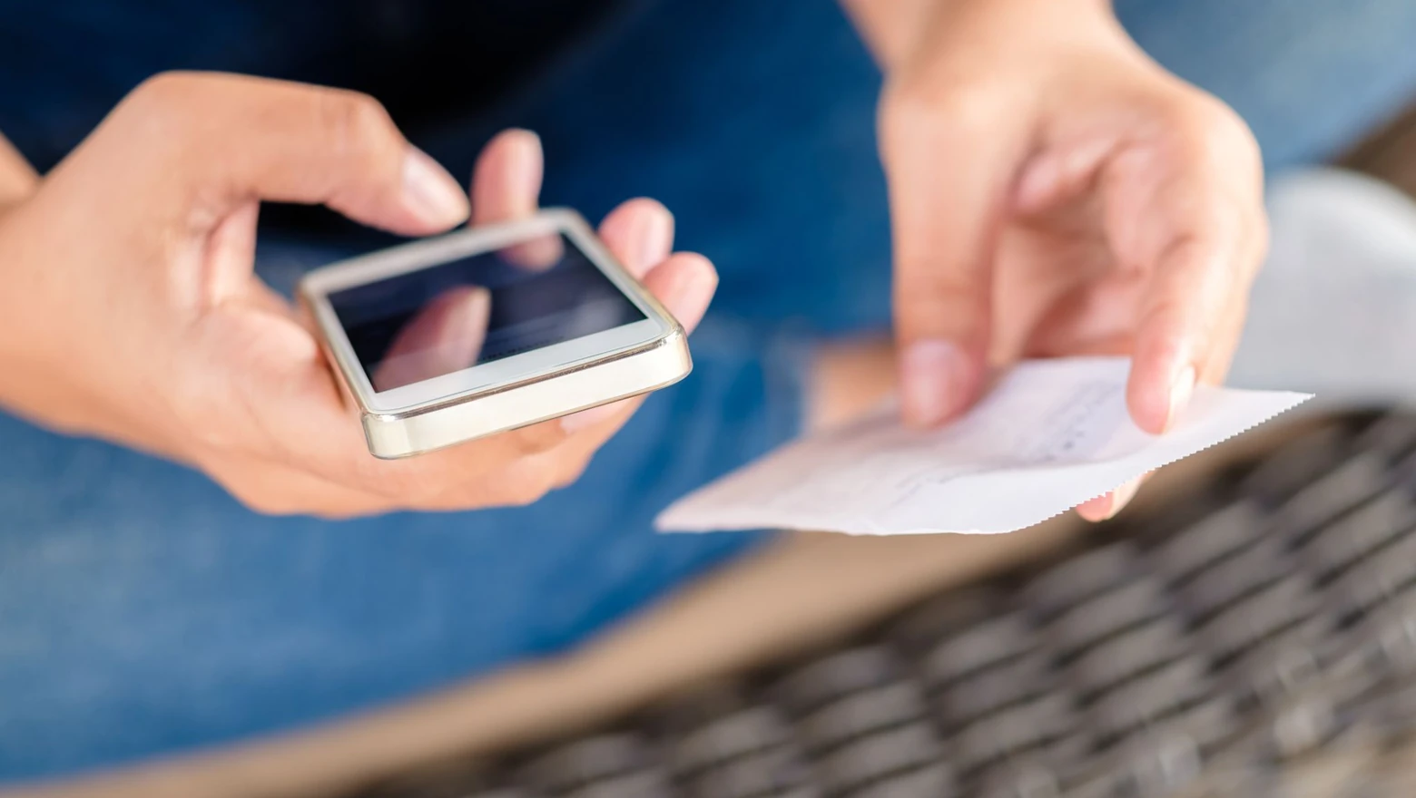 Close-up of hands holding a smartphone and a receipt while tracking expenses on the go.