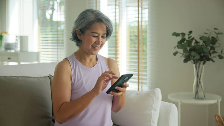 A woman smiling as she uses Coach Chat on her smartphone while seated on a sofa at home.