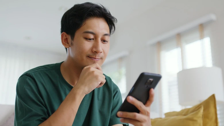 A man thoughtfully reviews his credit score on a smartphone while comparing credit tools at home.