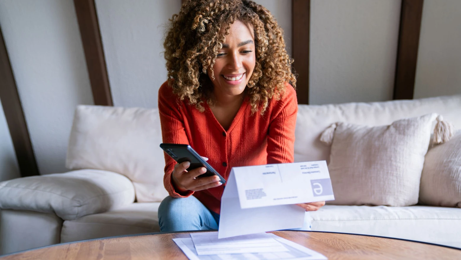 A woman reviews her credit and a bill on her phone while seated on a couch at home.
