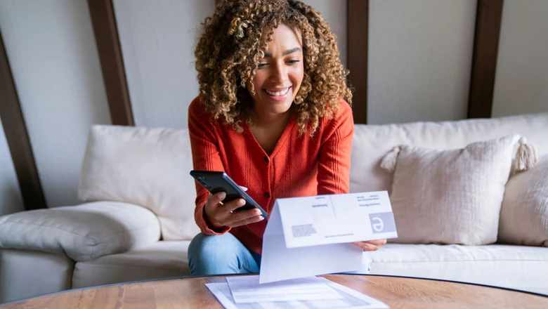 A woman reviews her credit and a bill on her phone while seated on a couch at home.
