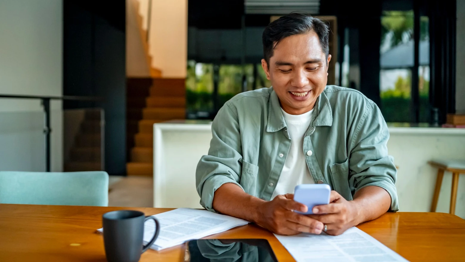 A smiling man checking his credit score on a smartphone at a bright dining table.