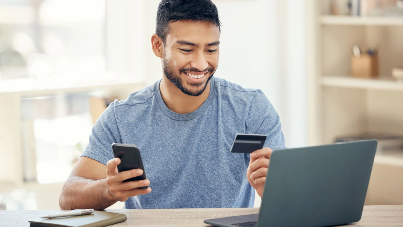 A smiling man checking his credit score on a laptop while holding a phone and credit card.