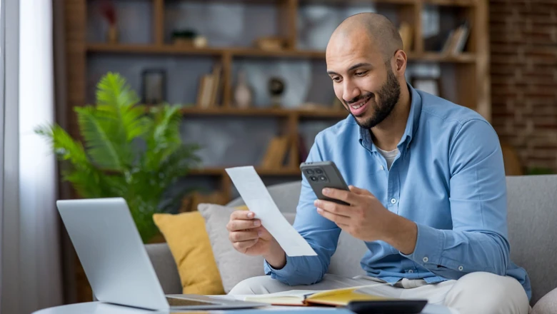 A man comparing Empower and SoFi Coach budgeting options on his phone at home with a laptop nearby.