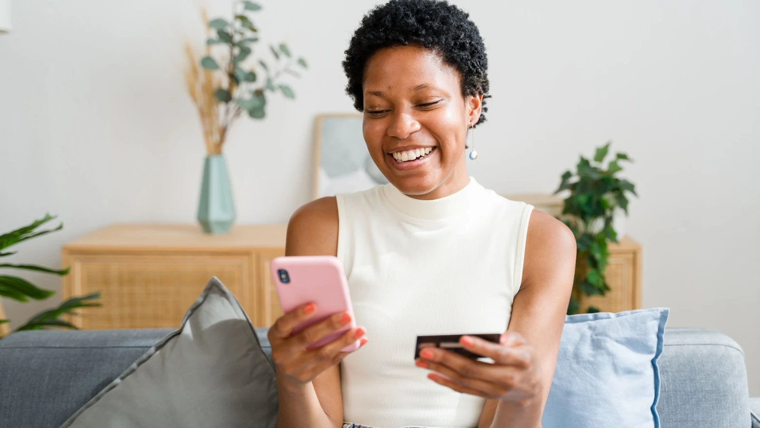 A smiling woman checking her credit score on a phone while holding a credit card.
