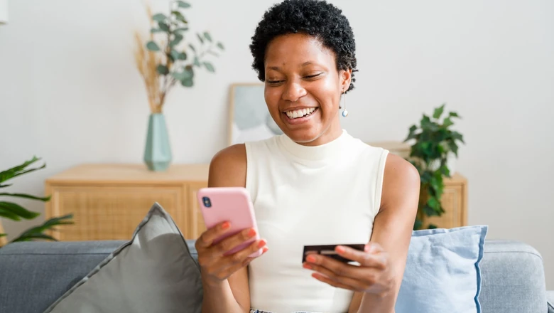 A smiling woman checking her credit score on a phone while holding a credit card.