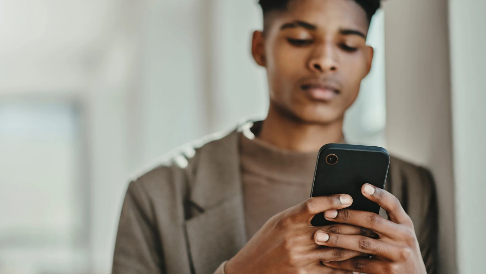 A man checking his credit score on a smartphone in a bright modern indoor space.