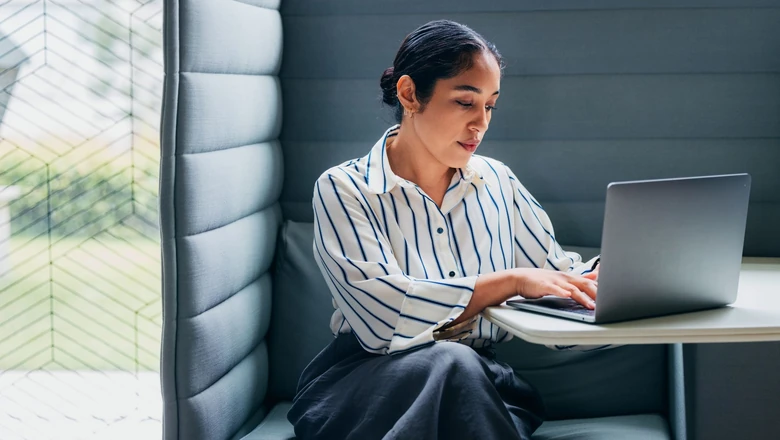 A woman researching Bitcoin halving on a laptop in an office booth.