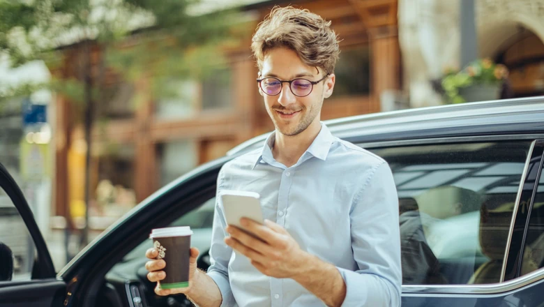 A man standing outside of a car and using his phone to research crypto custody.