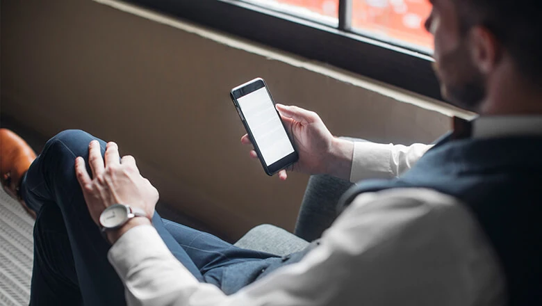 A man in a suit relaxing in a chair while researching backdoor Roth IRA options on his smartphone.