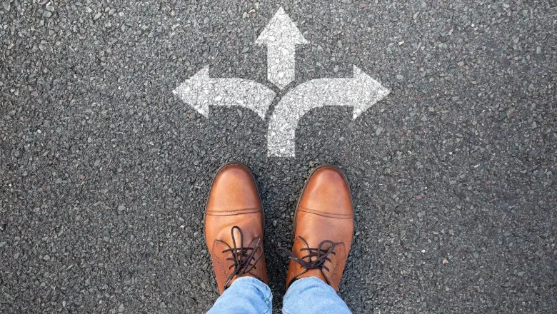 Person standing on pavement facing arrows pointing in multiple directions.
