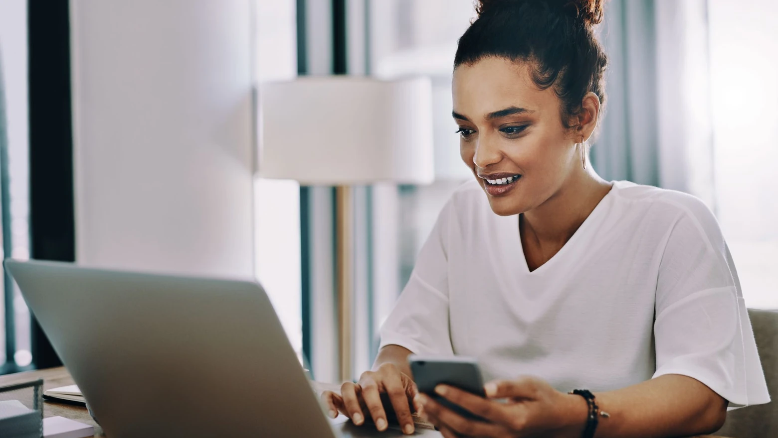 A woman comparing SoFi Plus and Robinhood Gold on a phone and laptop.