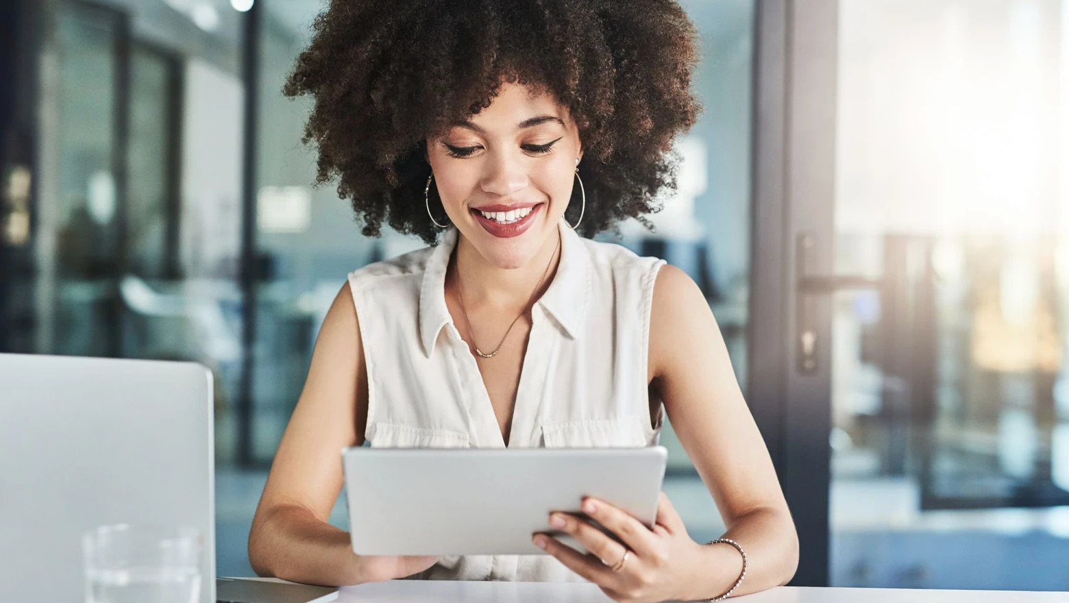 A woman at an office desk holding a tablet and researching SoFi Plus benefits and rewards.