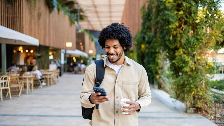 A man walking with a coffee and using his smartphone to research a SoFi Plus Membership.