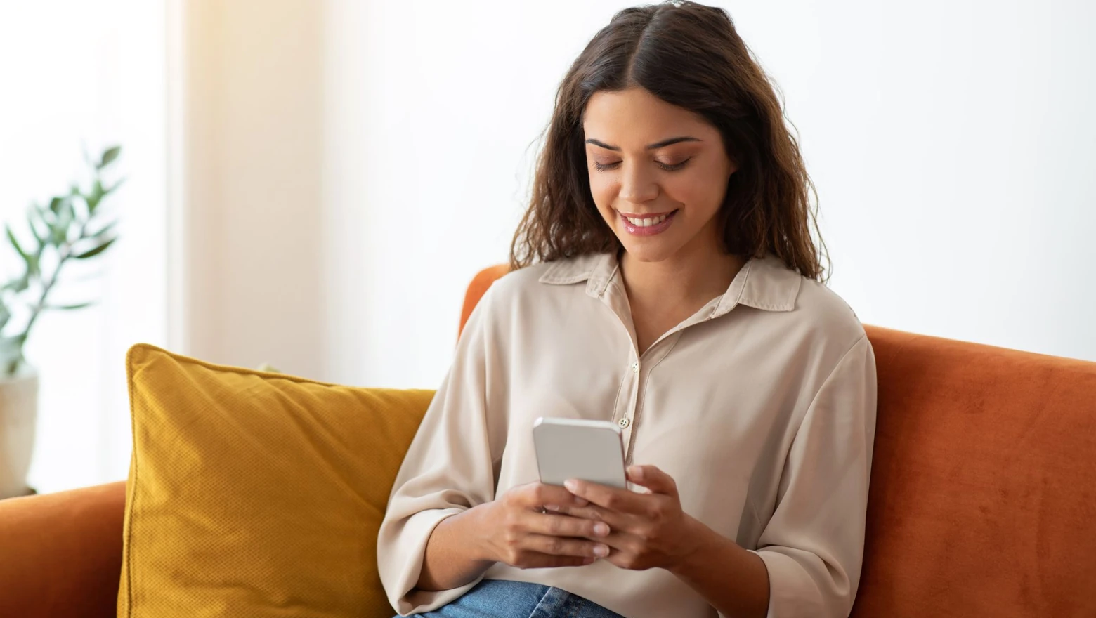 A woman smiling while using a phone to research if SoFi Plus is worth it.