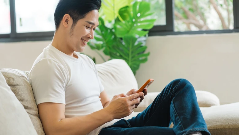 A smiling man on a sofa using a smartphone to compare SoFi Credit Card and Citi Double Cash card benefits.