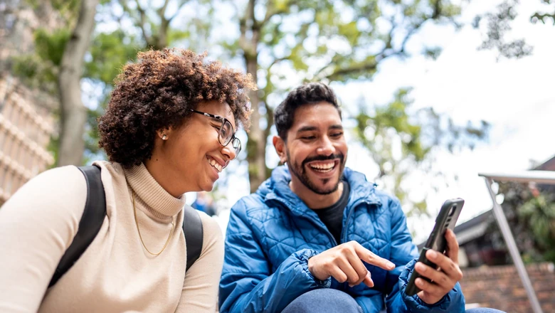 Two people smiling and using a smartphone to research SoFi Credit Card vs. Venmo Credit Card