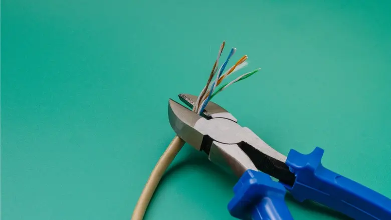 Wire cutters cutting through exposed electrical cable, symbolizing home electrical repair or rewiring work.