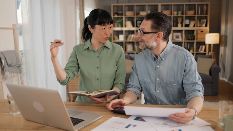 Two people discuss second chance loan options at a home desk with a laptop, notebook, and financial documents.