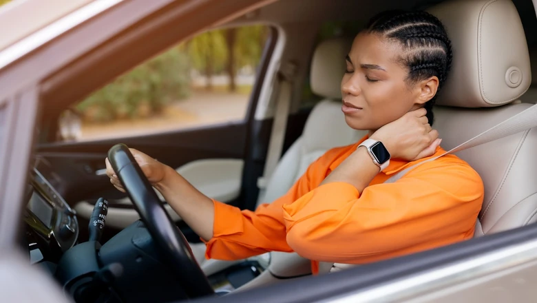 A woman in a car holding the back of her neck after an auto accident.