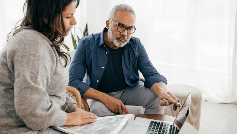 Two people in a living room looking at a laptop and notebook while discussing what happens to homeowners insurance after the owner dies.