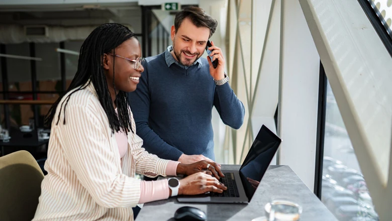 Two small business owners speaking on the phone and using a laptop to research payment processing.