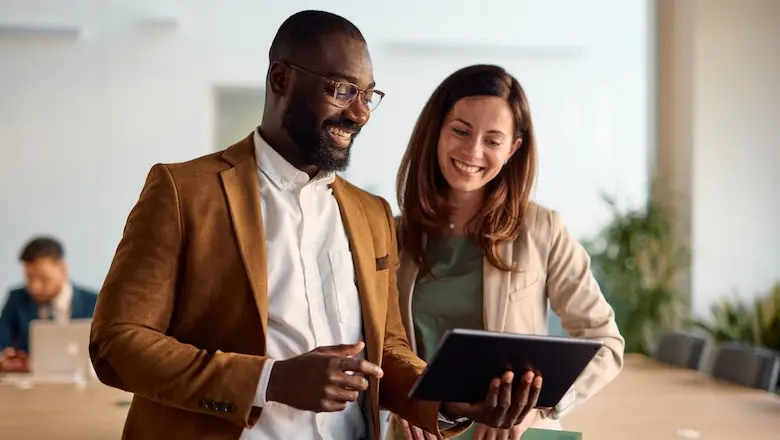 Two people in an office discussing the pros and cons of a limited liability company while looking at a tablet.