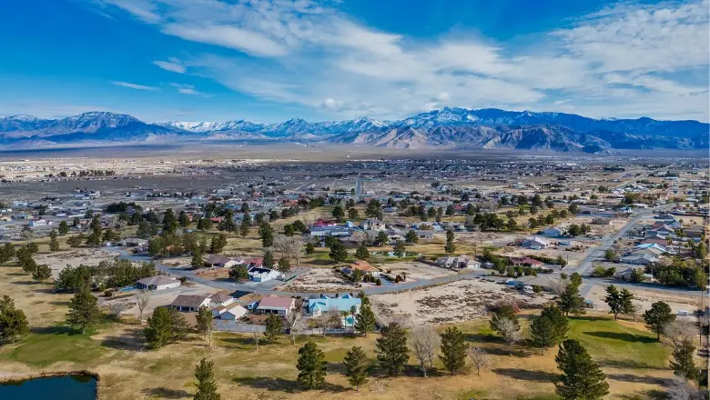 An aerial view of a suburban neighborhood and golf course with a snow-capped mountain range in the distance.