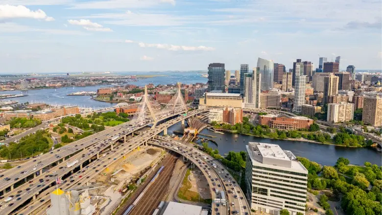 An aerial view of the Boston skyline, with busy highways, the Zakim Bridge, and the Charles River.