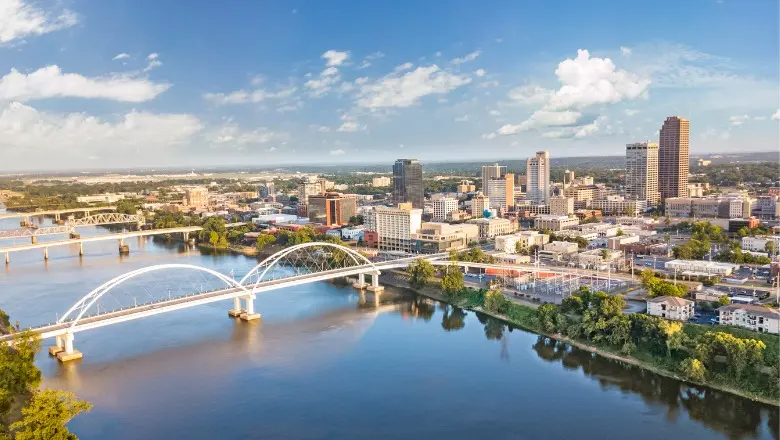 An aerial view of the downtown Little Rock skyline with the Arkansas River and a bridge in the foreground.