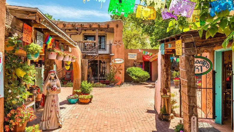 A street level view of Old Town Albuquerque, with historic adobe buildings and a church surrounding a plaza.

