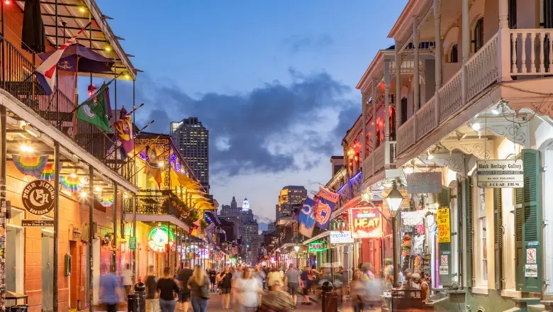 A busy New Orleans street scene at dusk, with crowds walking along the lively Bourbon Street.