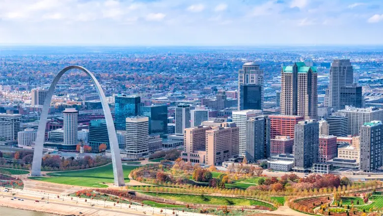 An aerial view of the St. Louis skyline, featuring the Gateway Arch and skyscrapers along the Mississippi River.