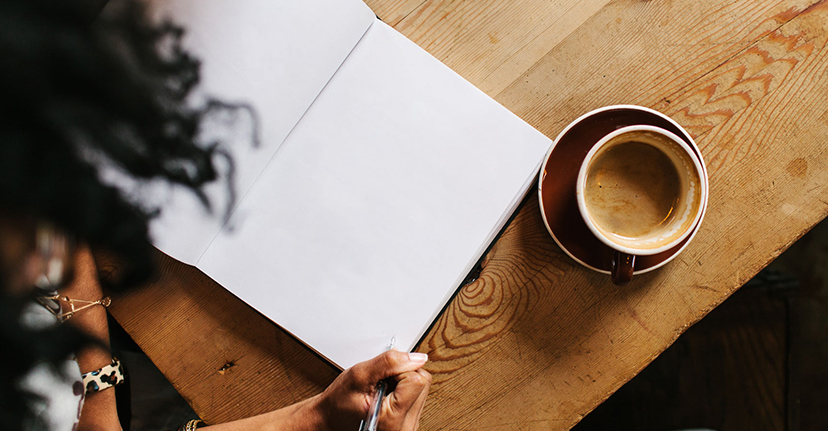 woman writing in notebook with coffee