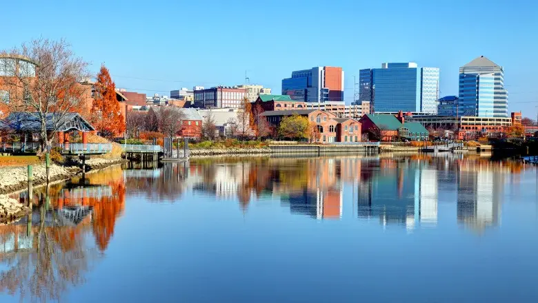 A clear daytime shot of the Wilmington, Delaware waterfront, with the city skyline reflecting on the calm water.